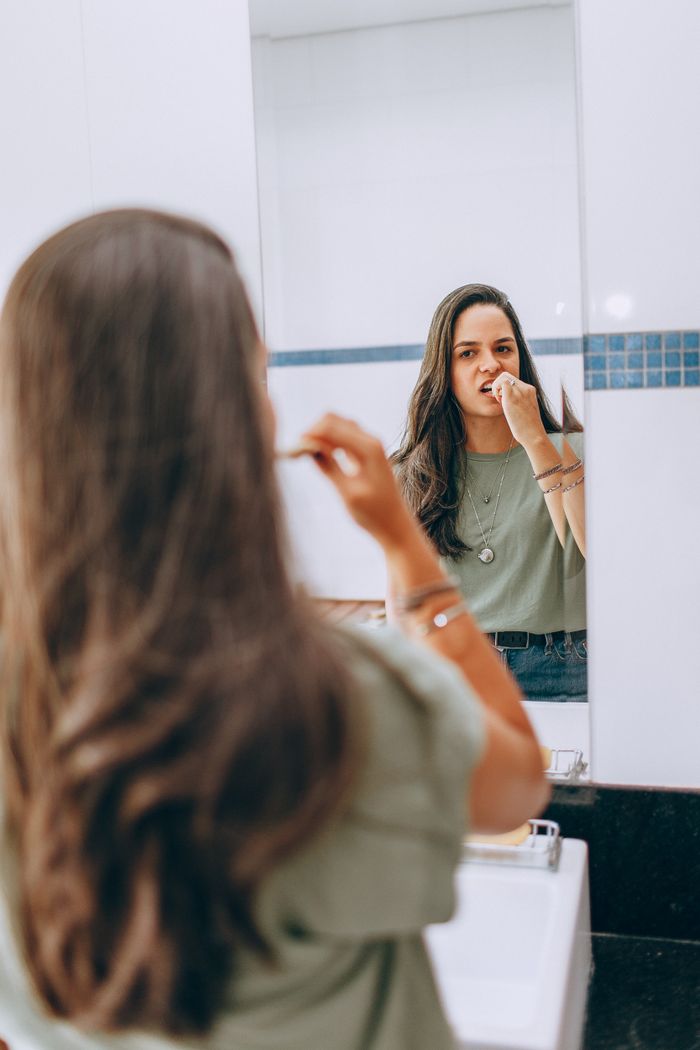 Young woman brushing teeth in a modern bathroom mirror with reflection.